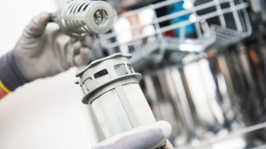 A gloved hand holding a piece of a dishwasher.