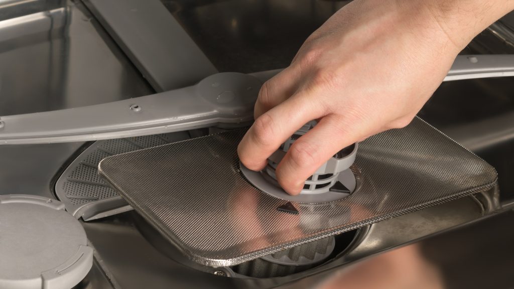 A hand servicing a commercial dishwasher.